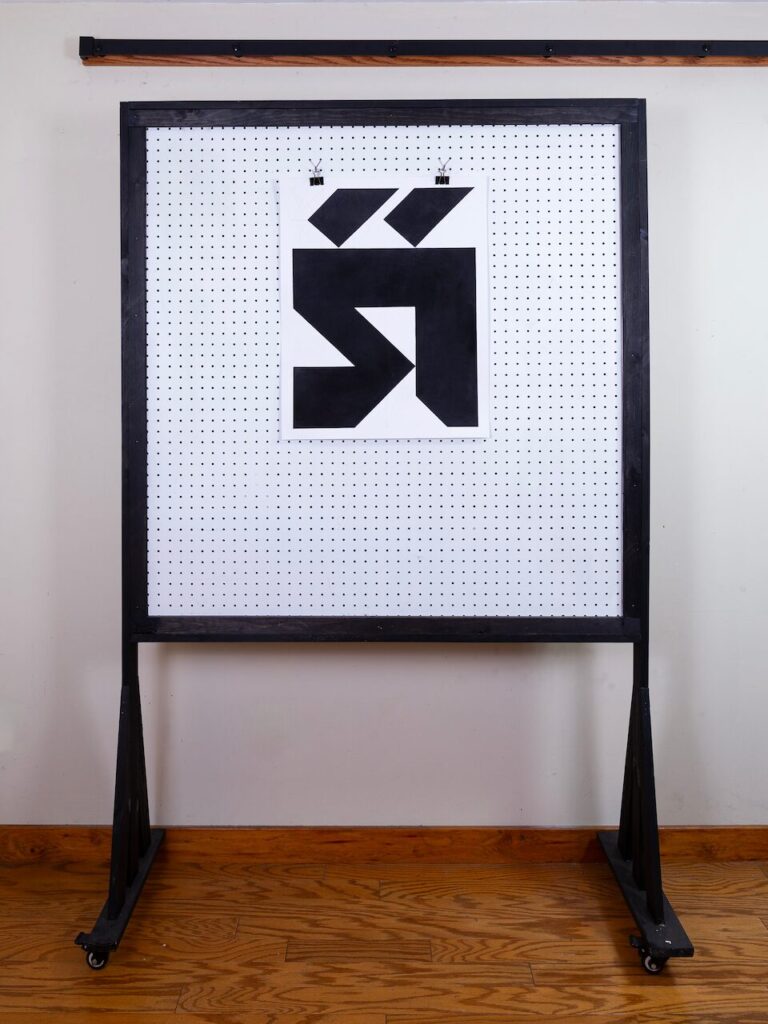 The drawing mounted on a pegboard wall in a studio setting, shown in a wide shot to provide scale.