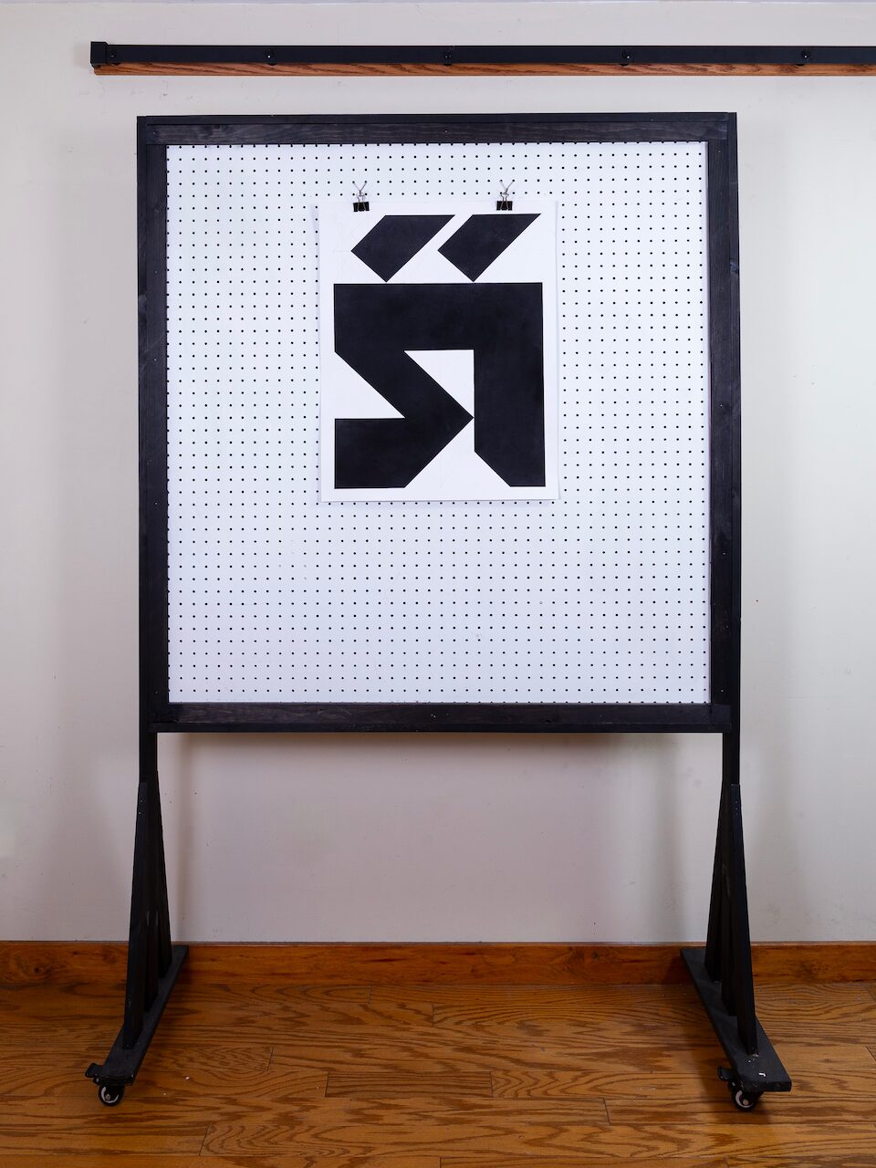 The drawing mounted on a pegboard wall in a studio setting, shown in a wide shot to provide scale.