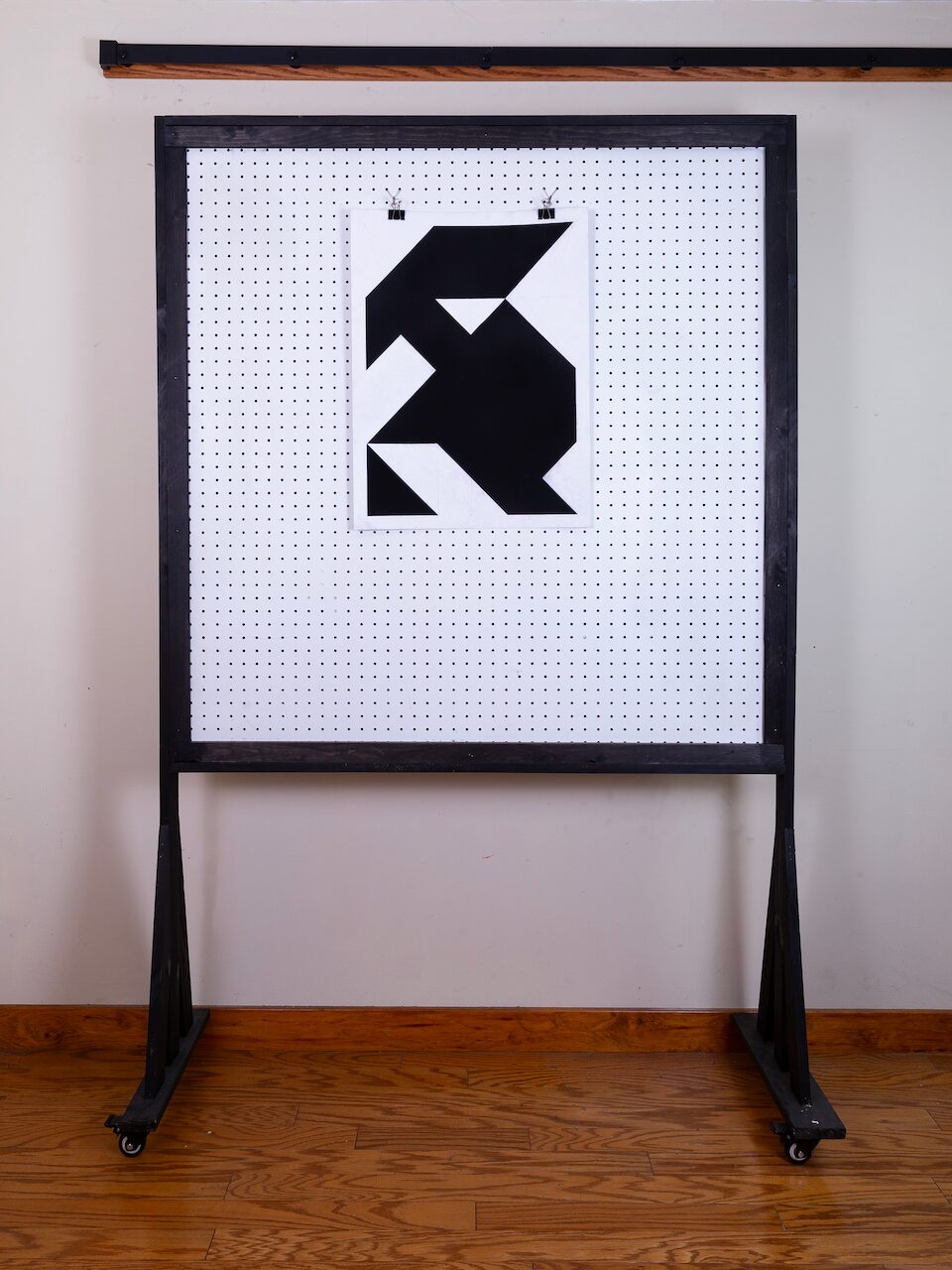 Caretaker (Glyph Drawing No. 5) displayed on studio pegboard, showing scale. Minimalist charcoal drawing with geometric forms and subtle figurative suggestion.