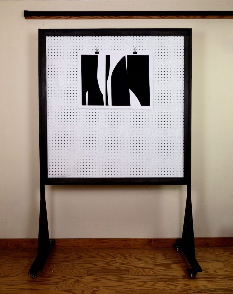 Studio shot of Formal Gathering, No. 1 mounted on pegboard, showing the scale of the landscape-format geometric drawing and its dark, textured charcoal surface.