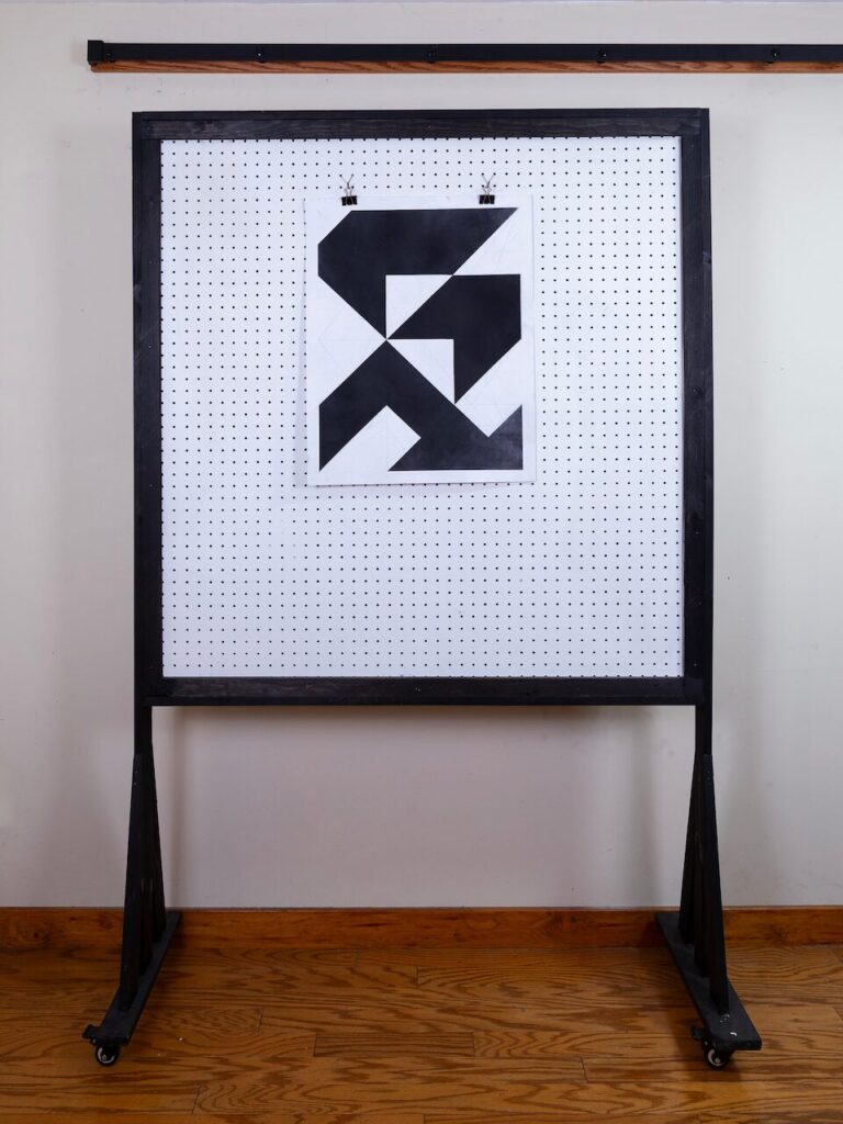 Wide view of Neighborhood, from the Air (Glyph Drawing No. 7) hanging on a studio pegboard, showing scale and texture of the abstract rooftops and shared driveway composition.