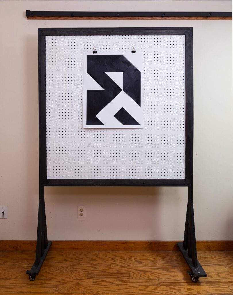Studio shot of Open House mounted on pegboard, showing the scale of the black-and-white geometric drawing and the smooth, brayered surface.