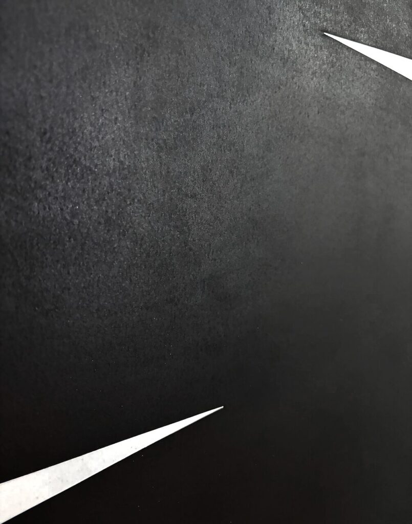 Detail of an abstract charcoal drawing, showing an ultra-smooth, even texture, interrupted by a sharp white triangular cut into the surface.