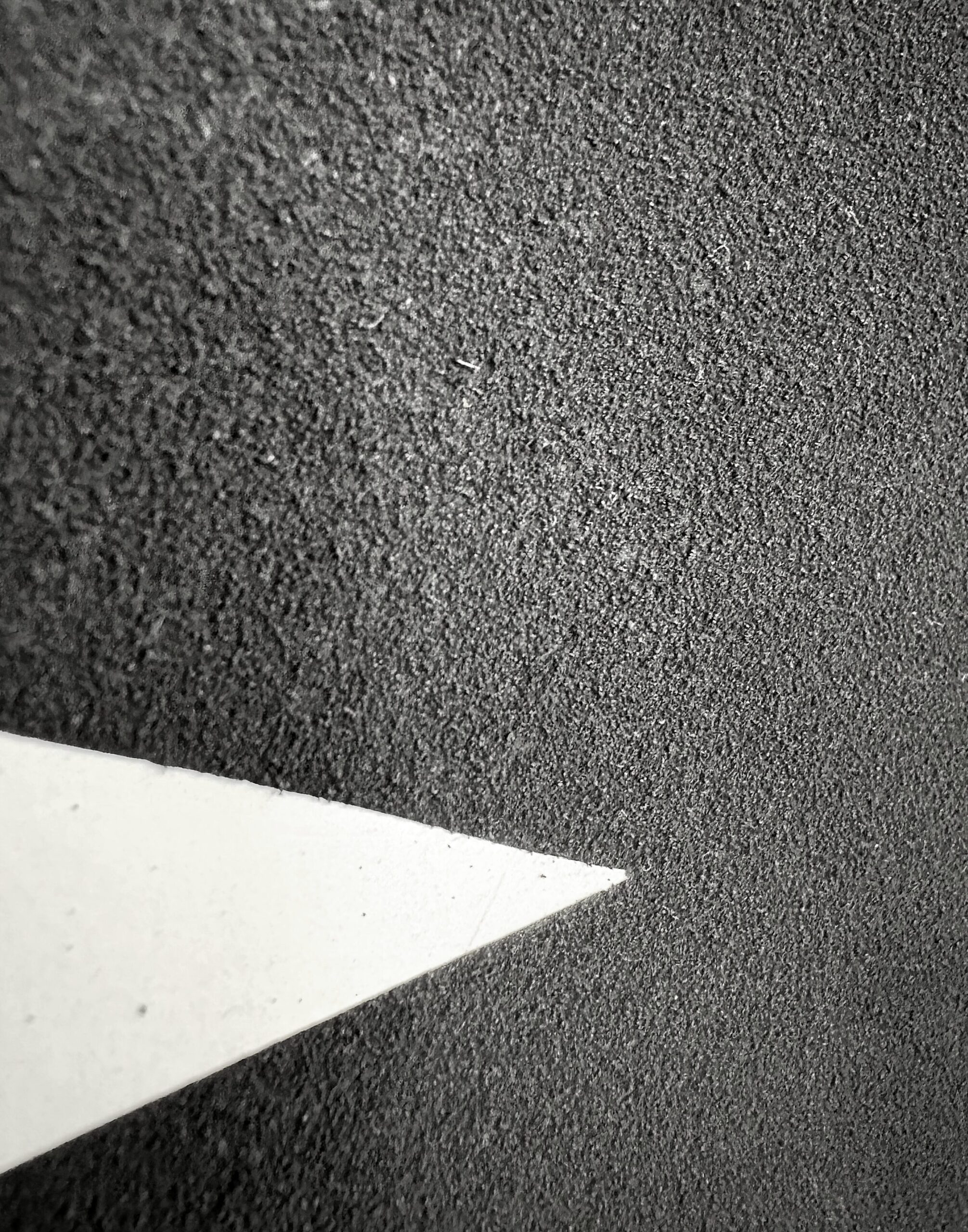 Detail of Untitled Drawing, No. 1, an abstract charcoal drawing, showing rich, even texture like fine sand, interrupted by a sharp white triangular cut into the surface.